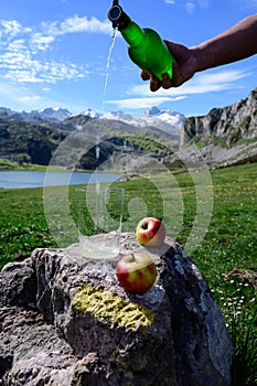 Pouring of natural Asturian cider made fromÂ fermented apples from green bottle and high height with view on Covadonga lake and